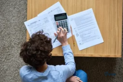 Une personne assise à une table, concentrée à faire ses calculs pour sa déclaration de revenus en France, utilisant une calculatrice et des formulaires.